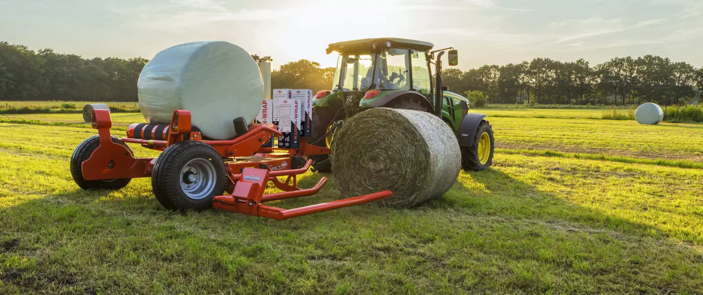 Прицепной рулонный обмотчик RW 1610 загружает один тюк во время упаковки другого.