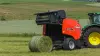 Рулонный пресс-подборщик KUHN FB 3130 производит тюк травы, обвязанный сеткой, в холмистой местности.