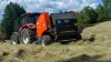 Стационарный рулонный пресс-подборщик KUHN FB 3125 с оператором в поле на заднем плане